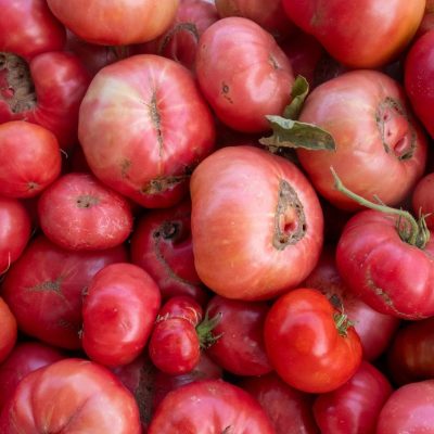 Close de tomates variados, com formas e texturas naturais, expostos em uma banca de feira.