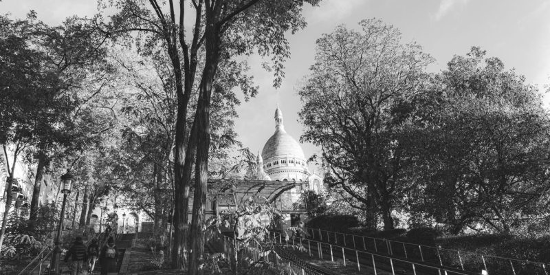 Vista em preto e branco da Basílica de Sacré-Cœur entre árvores, em Montmartre, Paris.