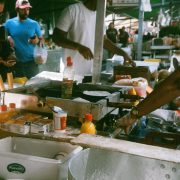 Público circula entre barracas de uma feira de comida em São Paulo, com vendedores e produtos expostos.