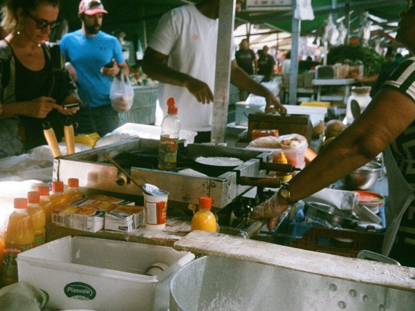 Público circula entre barracas de uma feira de comida em São Paulo, com vendedores e produtos expostos.