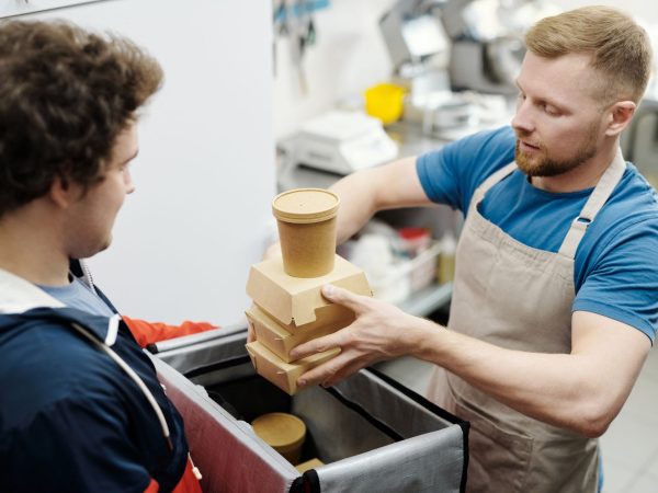 Funcionário de cozinha coloca recipientes de comida em uma bolsa para entrega.