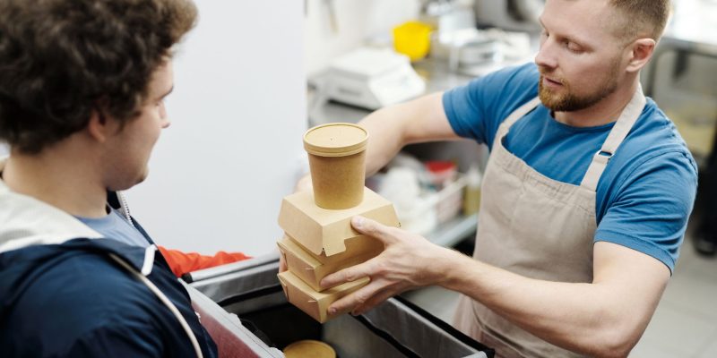 Funcionário de cozinha coloca recipientes de comida em uma bolsa para entrega.