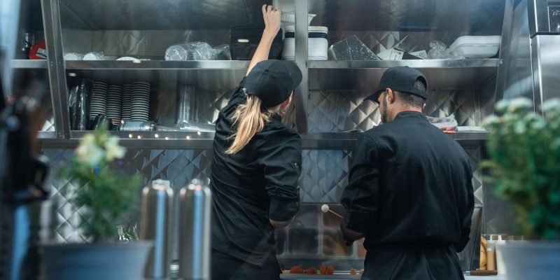 Dois chefs trabalham juntos no preparo de alimentos em uma cozinha profissional.